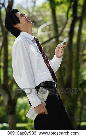 A man laughs as he checks his cellphone in the park View Large Photo Image Stock Image - A man laughs as he checks his cellphone in the park. Fotosearch