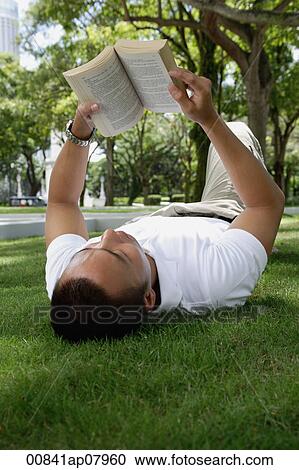 A man lies down and reads in the park View Large Photo Image Stock Image - A man lies down and reads in the park. Fotosearch