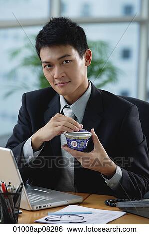 Stock Photograph - A man looks at the camera as he as he holds a Chinese tea cup. Fotosearch