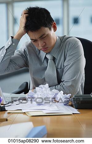 Stock Image - A man looks stressed as he works at his desk. Fotosearch