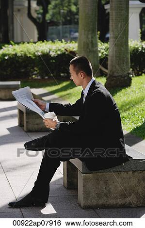 Stock Photograph - A man sits and reads the newspaper in the park. Fotosearch