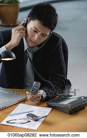 A man sits at his desk with lots of phones View Large Photo Image Stock Image - A man sits at his desk with lots of phones. Fotosearch