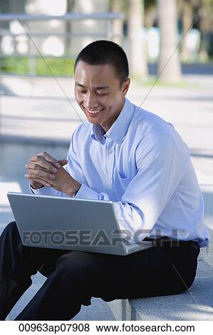 Stock Photo - A man smiles as he uses his laptop outdoors. Fotosearch