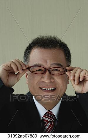 A man smiles at the camera as he puts on his glasses View Large Photo Image Stock Photo - A man smiles at the camera as he puts on his glasses. Fotosearch
