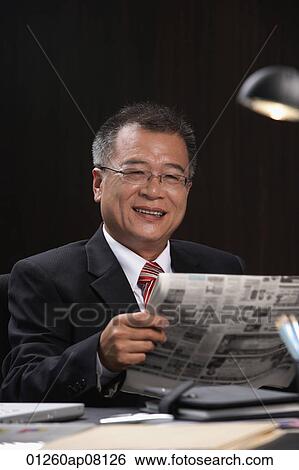 A man smiles at the camera as he reads the newspaper at work View Large Photo Image Stock Photograph - A man smiles at the camera as he reads the newspaper at work. Fotosearch