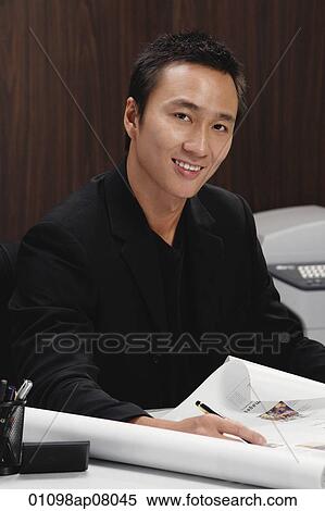 A man smiles at the camera as he rolls out plans on his desk View Large Photo Image Stock Photography - A man smiles at the camera as he rolls out plans on his desk. Fotosearch