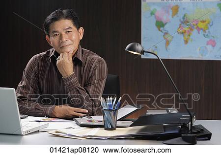A man smiles at the camera as he sits at his desk View Large Photo Image Stock Image - A man smiles at the camera as he sits at his desk. Fotosearch