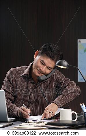A man talks on the phone as he works View Large Photo Image Stock Image - A man talks on the phone as he works. Fotosearch