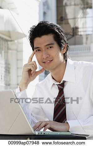 A man uses his laptop outside while he looks at the camera View Large Photo Image Stock Photo - A man uses his laptop outside while he looks at the camera. Fotosearch