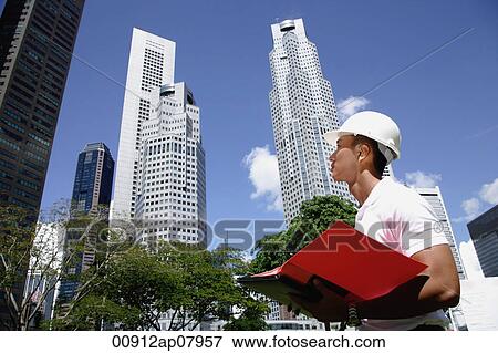 A man with a helmet stands in front of skyscrapers View Large Photo Image Stock Photo - A man with a helmet stands in front of skyscrapers. Fotosearch
