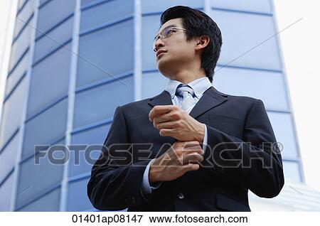Stock Photo - A man with a suit stands in front of a skyscraper. Fotosearch