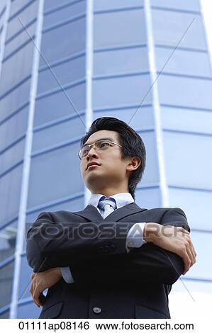 Stock Photograph - A man with a suit stands in front of a skyscraper. Fotosearch