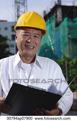 A man with a yellow helmet smiles at the camera, holding file View Large Photo Image Stock Image - A man with a yellow helmet smiles at the camera, holding file. Fotosearch