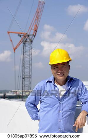 A man with a yellow helmet smiles at the camera as he works View Large Photo Image Stock Photography - A man with a yellow helmet smiles at the camera as he works. Fotosearch