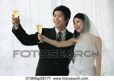 Stock Photo - A newlywed couple hold out their champagne glasses for a toast. Fotosearch