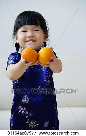 Stock Photo - A small girl holds out two mandarin oranges. Fotosearch