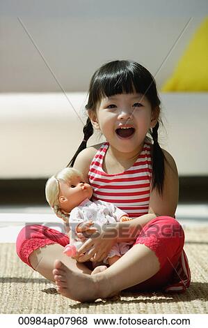 A small girl plays with a doll as she looks at the camera View Large Photo Image Stock Photo - A small girl plays with a doll as she looks at the camera. Fotosearch