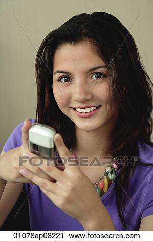 A teenage girl smiles at the camera as she uses her cellphone View Large Photo Image Stock Image - A teenage girl smiles at the camera as she uses her cellphone. Fotosearch