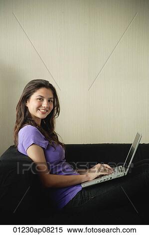 A teenage girl smiles at the camera as she uses a laptop View Large Photo Image Stock Photography - A teenage girl smiles at the camera as she uses a laptop. Fotosearch
