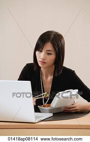 A woman eats lunch at her desk while she works View Large Photo Image Picture - A woman eats lunch at her desk while she works. Fotosearch