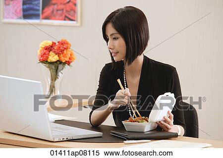 A woman eats lunch at her desk while she works View Large Photo Image Stock Photography - A woman eats lunch at her desk while she works. Fotosearch