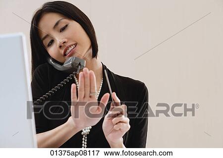 A woman files her nails as she talks on the phone at work View Large Photo Image Stock Photo - A woman files her nails as she talks on the phone at work. Fotosearch