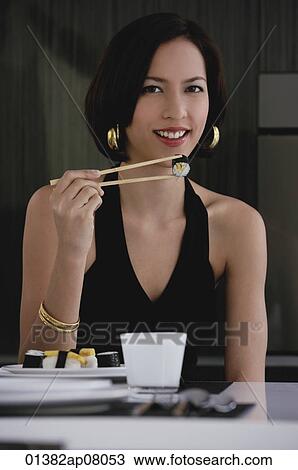 A woman looks at the camera as she eats sushi View Large Photo Image Stock Image - A woman looks at the camera as she eats sushi. Fotosearch
