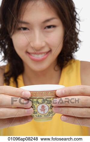 A woman looks at the camera as she holds out a cup of tea View Large Photo Image Stock Photo - A woman looks at the camera as she holds out a cup of tea. Fotosearch