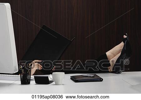 A woman puts her feet up on her desk as she reads from a folder View Large Photo Image Stock Photograph - A woman puts her feet up on her desk as she reads from a folder. Fotosearch