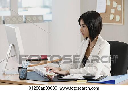 A woman sits at her desk and works View Large Photo Image Stock Image - A woman sits at her desk and works. Fotosearch