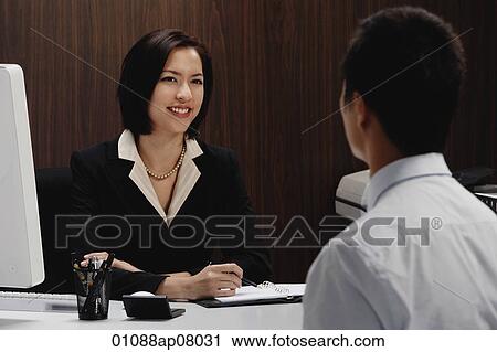 Stock Image - A woman sits at her desk while she talks with a man. Fotosearch