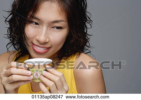 Stock Photo - A woman smiles as she has a cup of tea. Fotosearch