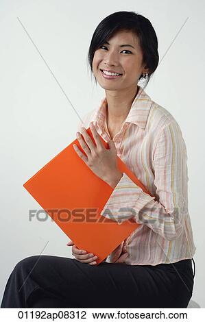 Stock Image - A woman smiles at the camera as she holds an orange folder. Fotosearch