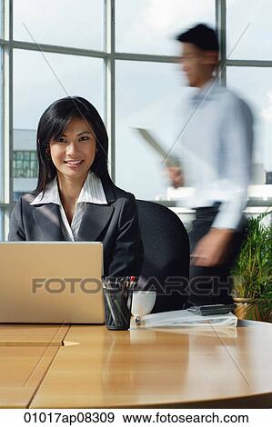 A woman smiles at the camera as she sits at her desk View Large Photo Image Stock Photo - A woman smiles at the camera as she sits at her desk. Fotosearch