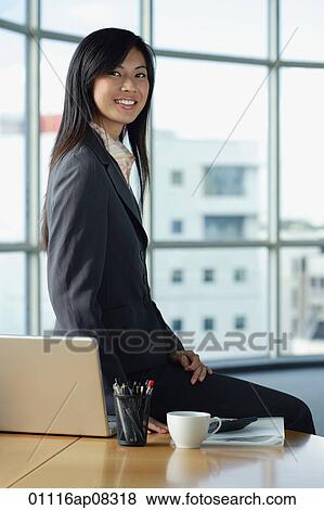 Stock Photo - A woman smiles at the camera as she sits on her desk. Fotosearch