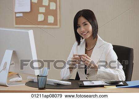 A woman smiles at the camera as she drinks a cup of tea at work View Large Photo Image Stock Photo - A woman smiles at the camera as she drinks a cup of tea at work. Fotosearch