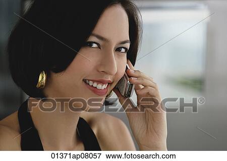 A woman smiles at the camera as she talks on her cellphone View Large Photo Image Stock Photo - A woman smiles at the camera as she talks on her cellphone. Fotosearch