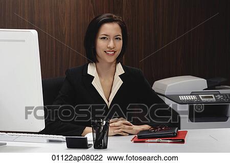 A woman smiles at the camera while she works at her desk View Large Photo Image Stock Image - A woman smiles at the camera while she works at her desk. Fotosearch