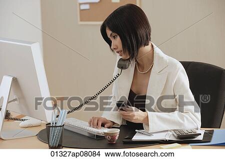 Picture - A woman talks on the phone while she is at work. Fotosearch