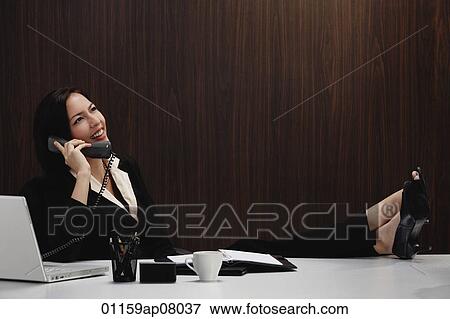 A woman talks on the phone while she is at her desk View Large Photo Image Stock Photo - A woman talks on the phone while she is at her desk. Fotosearch