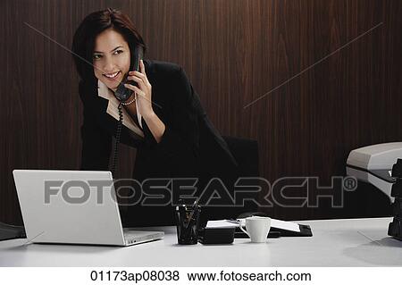 A woman talks on the phone while she is at her desk View Large Photo Image Stock Photo - A woman talks on the phone while she is at her desk. Fotosearch