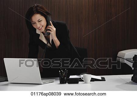A woman talks on the phone while she is at her desk View Large Photo Image Stock Photo - A woman talks on the phone while she is at her desk. Fotosearch