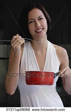 A woman tastes her cooking as she looks at the camera View Large Photo Image Stock Photo - A woman tastes her cooking as she looks at the camera. Fotosearch