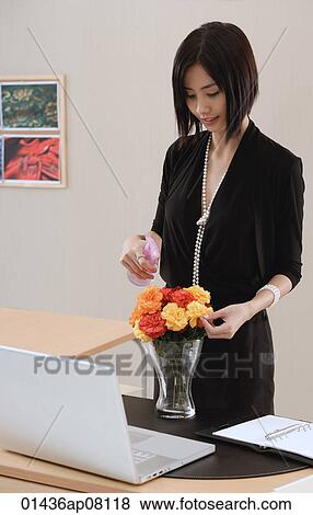 A woman tends to a vase of flowers on her desk at work View Large Photo Image Stock Photo - A woman tends to a vase of flowers on her desk at work. Fotosearch
