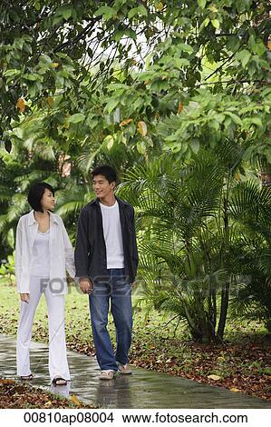 A young couple hold hands and stroll down a garden path together View Large Photo Image Picture - A young couple hold hands and stroll down a garden path together. Fotosearch