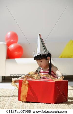 Stock Photograph - A young girl unwraps a birthday present. Fotosearch