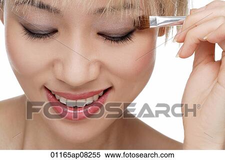 Stock Photography - A young woman applies eye shadow. Fotosearch