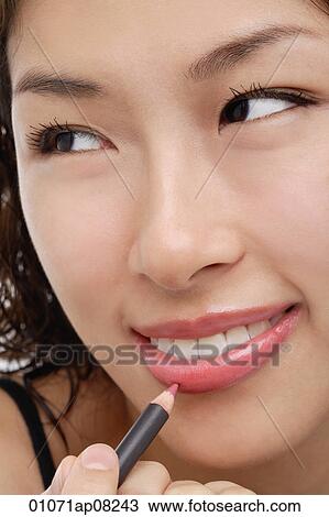 Stock Image - A young woman applies lip pencil. Fotosearch