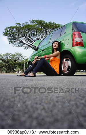 A young woman sits on the ground leaning against a car View Large Photo Image Stock Photo - A young woman sits on the ground leaning against a car. Fotosearch