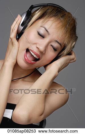 A young woman with headphones on listens to music View Large Photo Image Stock Image - A young woman with headphones on listens to music. Fotosearch